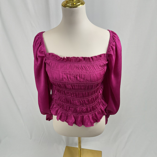 A magenta pink smocked blouse with puff sleeves and a ruffled hem, displayed on a cream mannequin torso with a gold stand against a white draped fabric background.