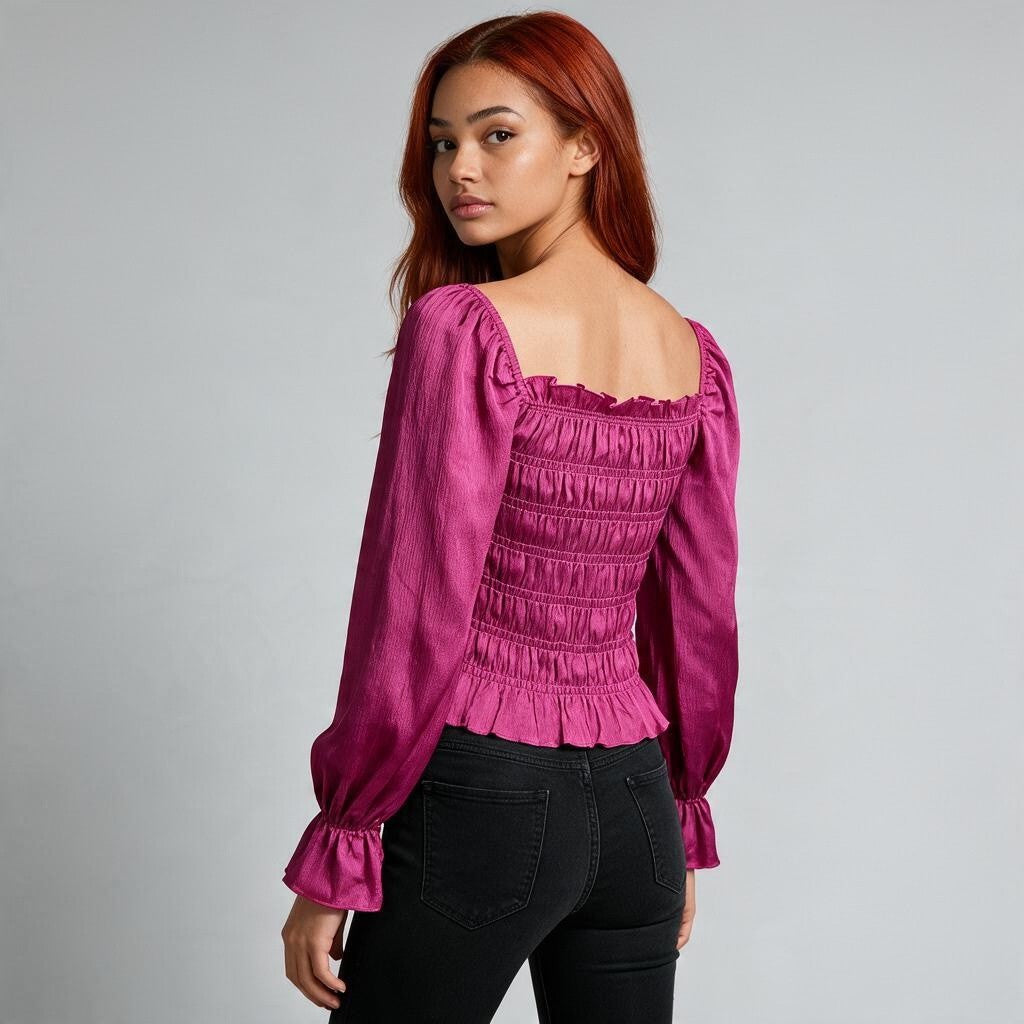 A woman with red hair wearing a magenta long-sleeve smocked blouse and black jeans, photographed from the back against a light gray studio background.
