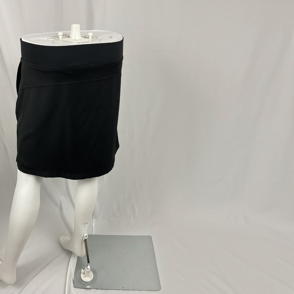 A black athletic mini skirt displayed on a white mannequin torso and legs against a white studio backdrop.