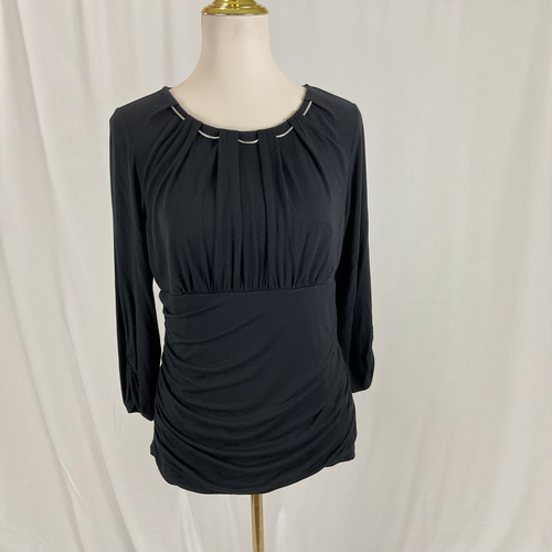 A black long-sleeve top with a gathered, pleated neckline and ruched waist, displayed on a cream mannequin torso against a white draped fabric background.