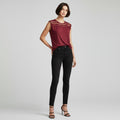 A model wearing a sleeveless burgundy top with a lace yoke and black skinny jeans, standing against a light gray studio background.
