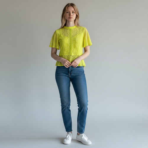 Woman wearing a yellow lace top and blue jeans against a plain background