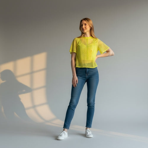 Woman wearing a yellow top and blue jeans standing in a well-lit room with a neutral background