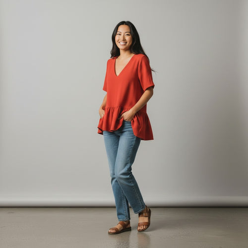 Woman wearing a red blouse and blue jeans standing against a plain background